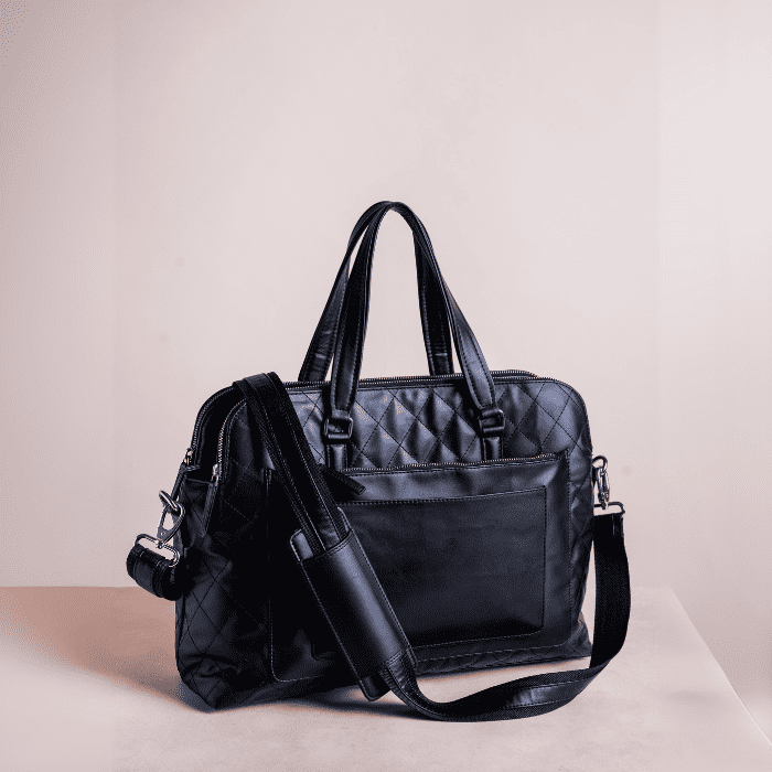 Black quilted vegan leather handbag with a shoulder strap on a light beige background