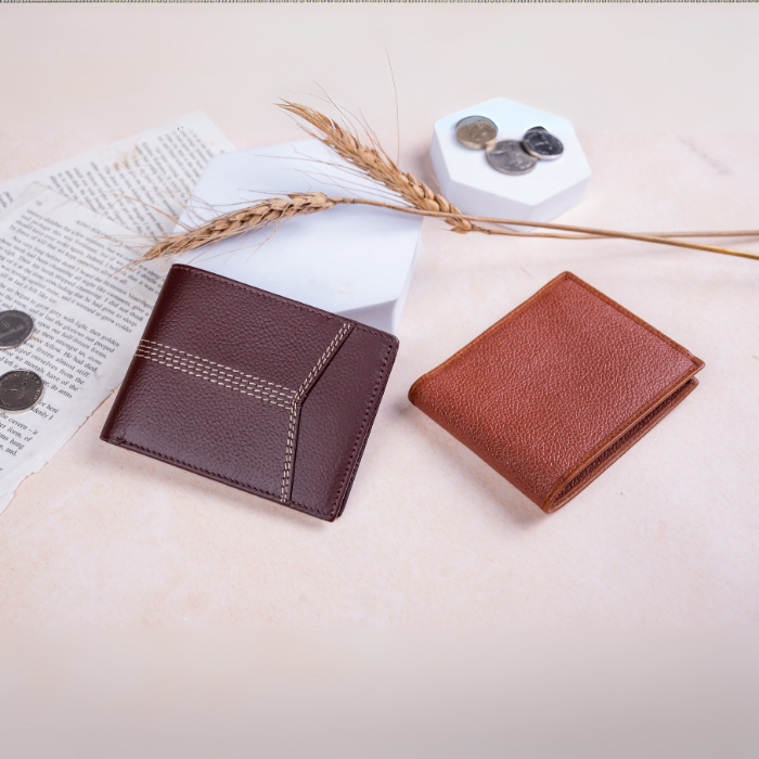 Two brown vegan leather wallets for men on a light surface with an open book and wheat stalks.
