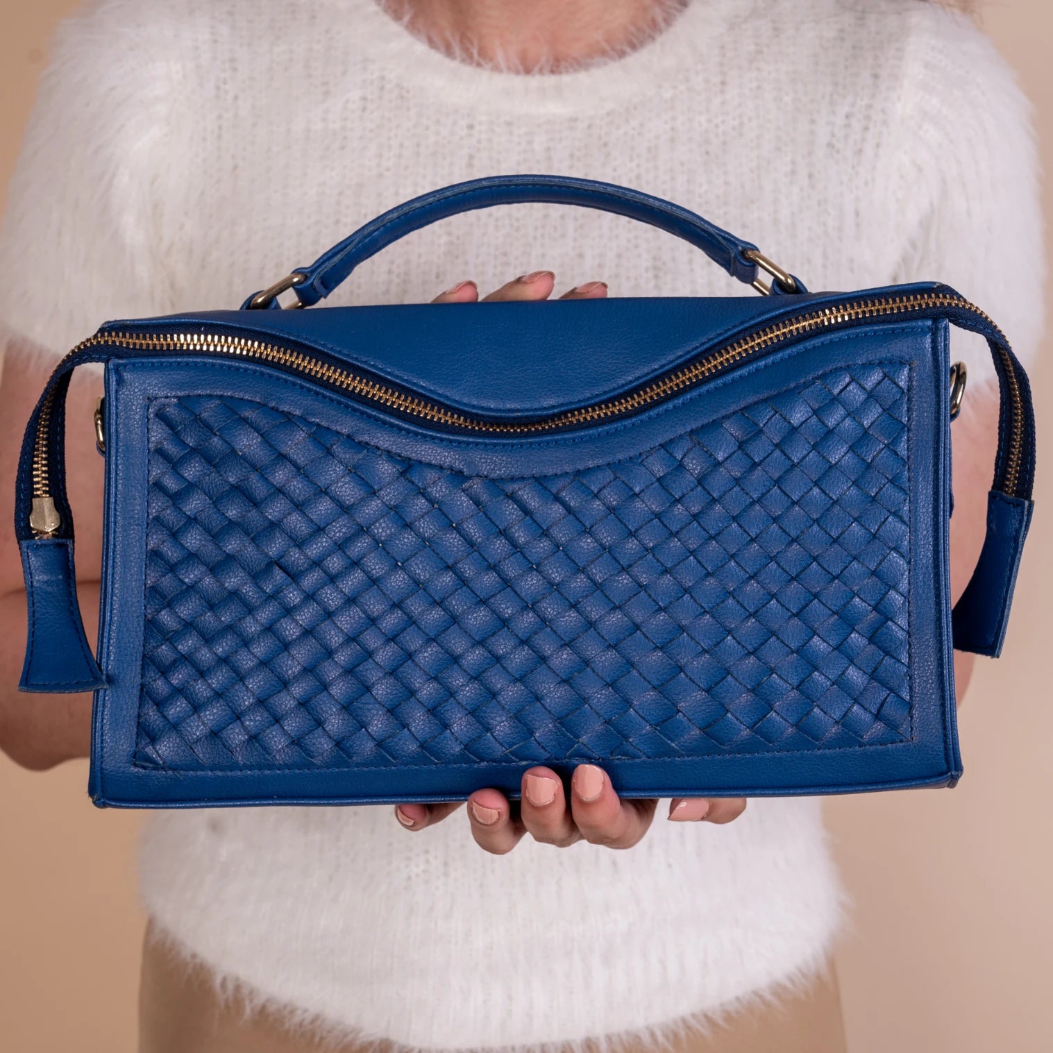 Blue woven vegan leather handbag for women held by a person wearing a white sweater.
