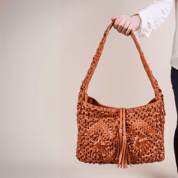 Brown woven leather handbag for women with tassel held by a person against a neutral background