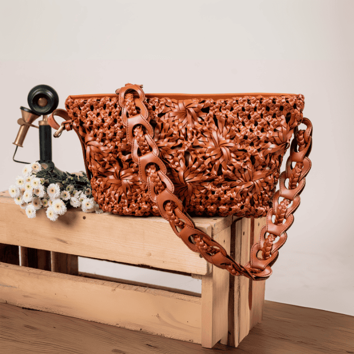 Carved vegan leather handbag for women with floral patterns on a wooden crate against a plain background