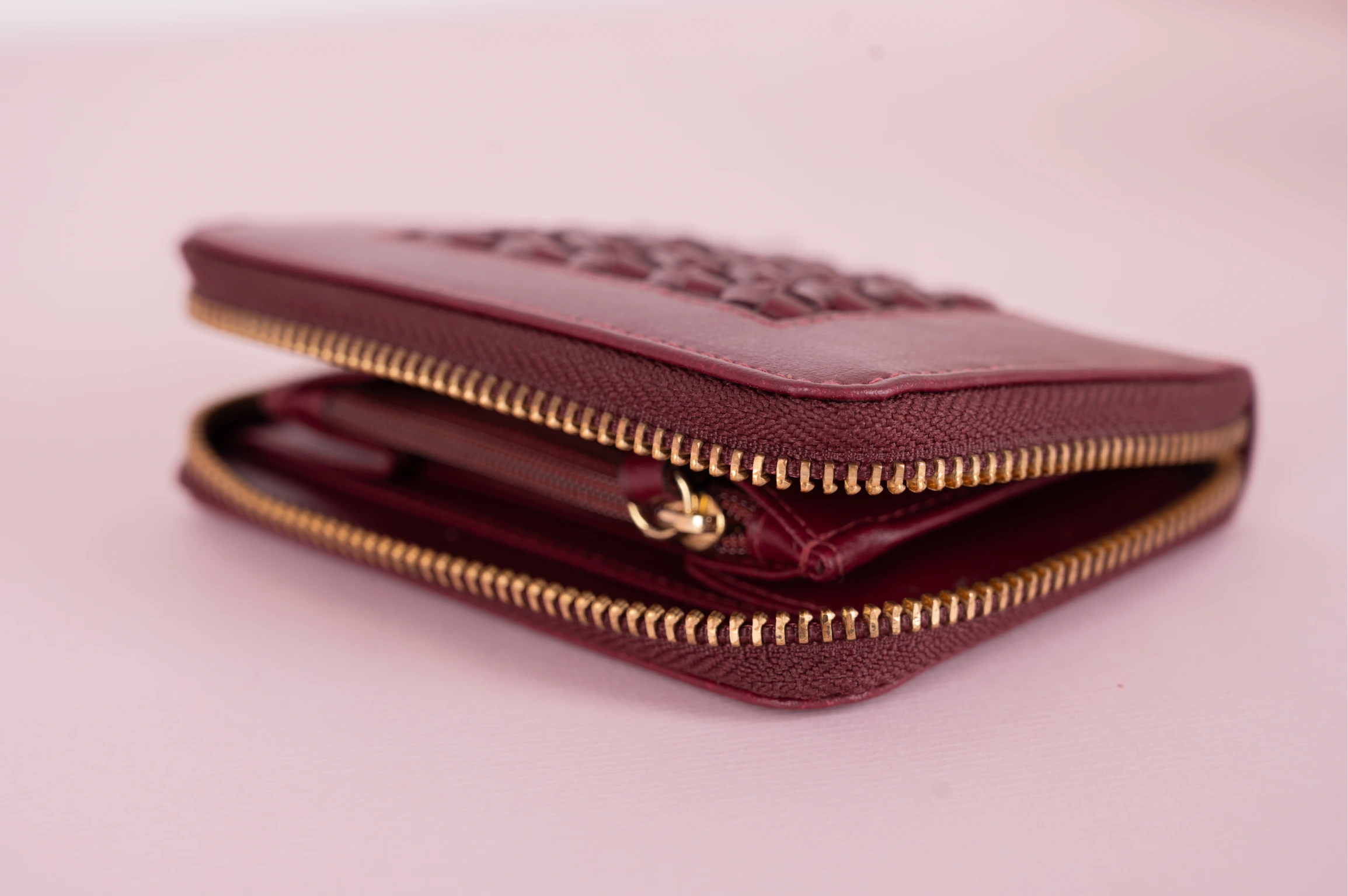 Maroon vegan leather wallet for women with gold zipper on a pink background
