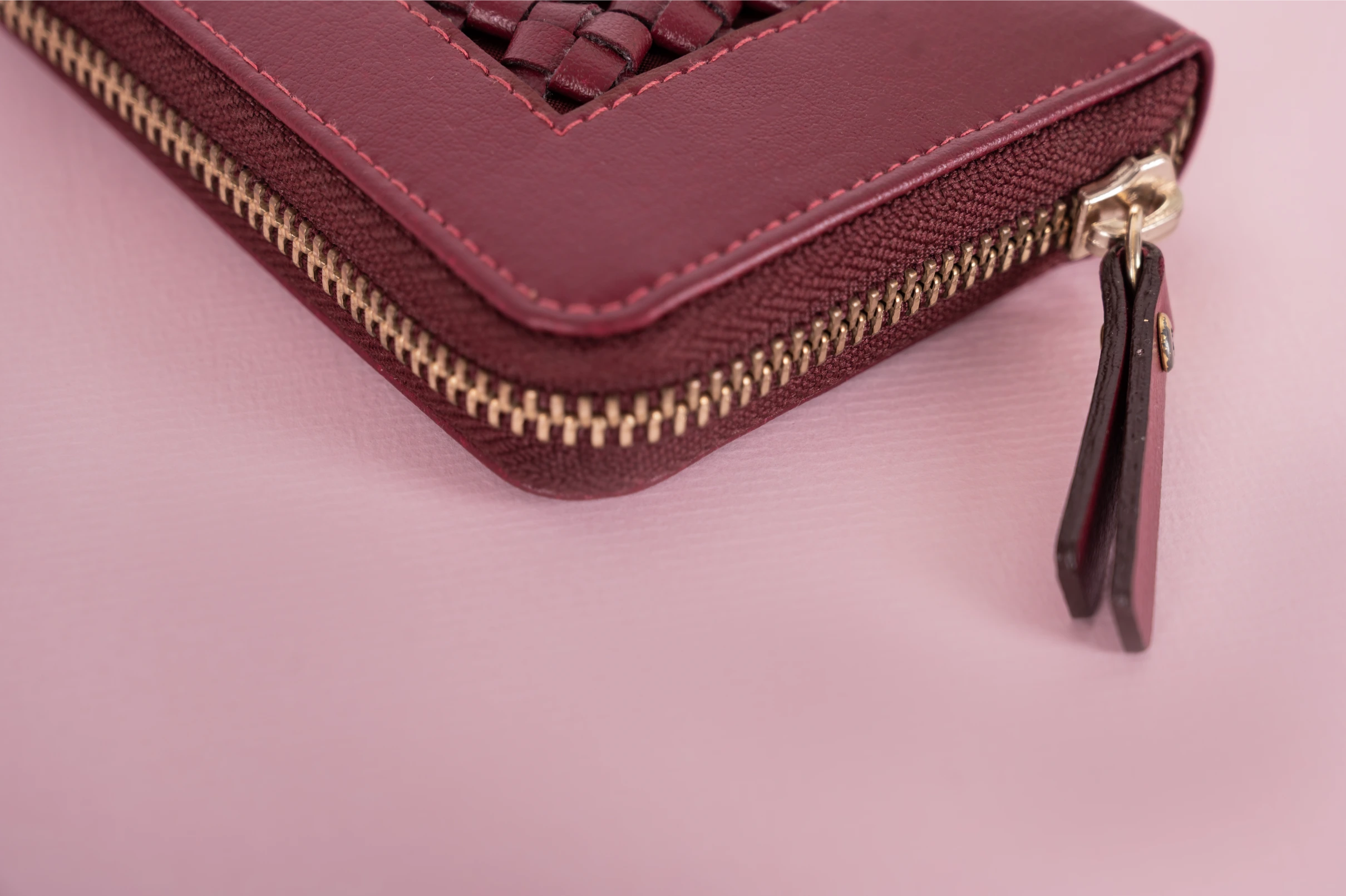 Maroon vegan leather wallet for women with gold zipper on a pink background
