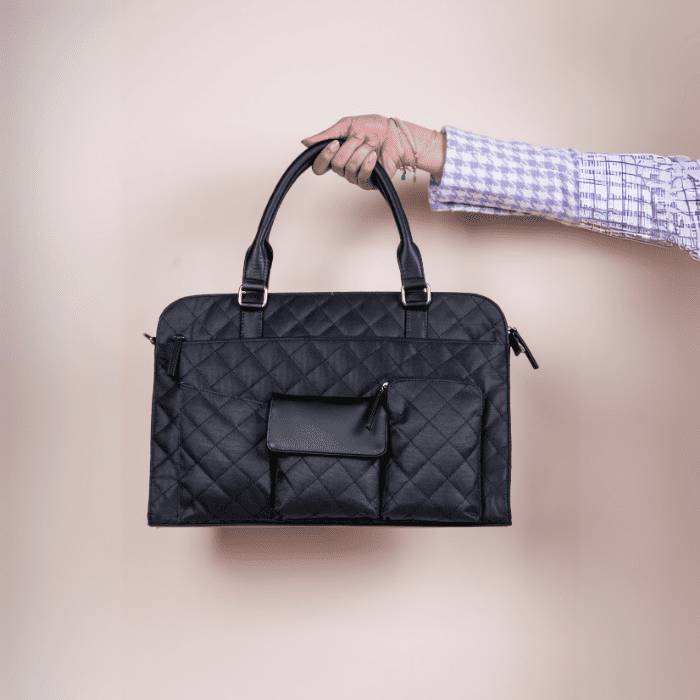 Black quilted vegan leather laptop bag held by a person against a beige background