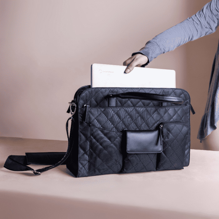 Black quilted vegan leather laptop bag with a person reaching in to place a white laptop inside on a beige background