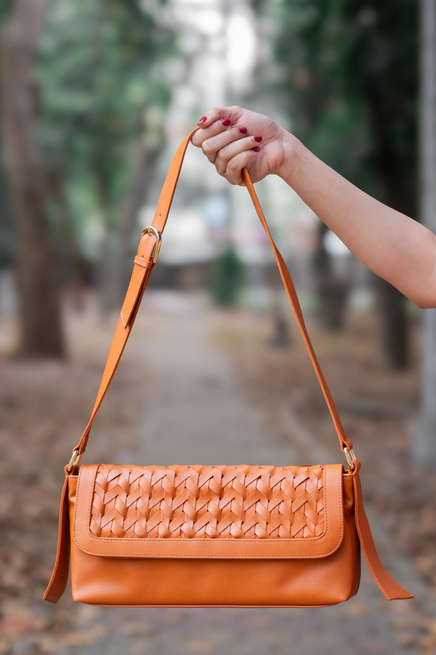 Orange woven vegan leather handbag for women held by a hand with blurred background