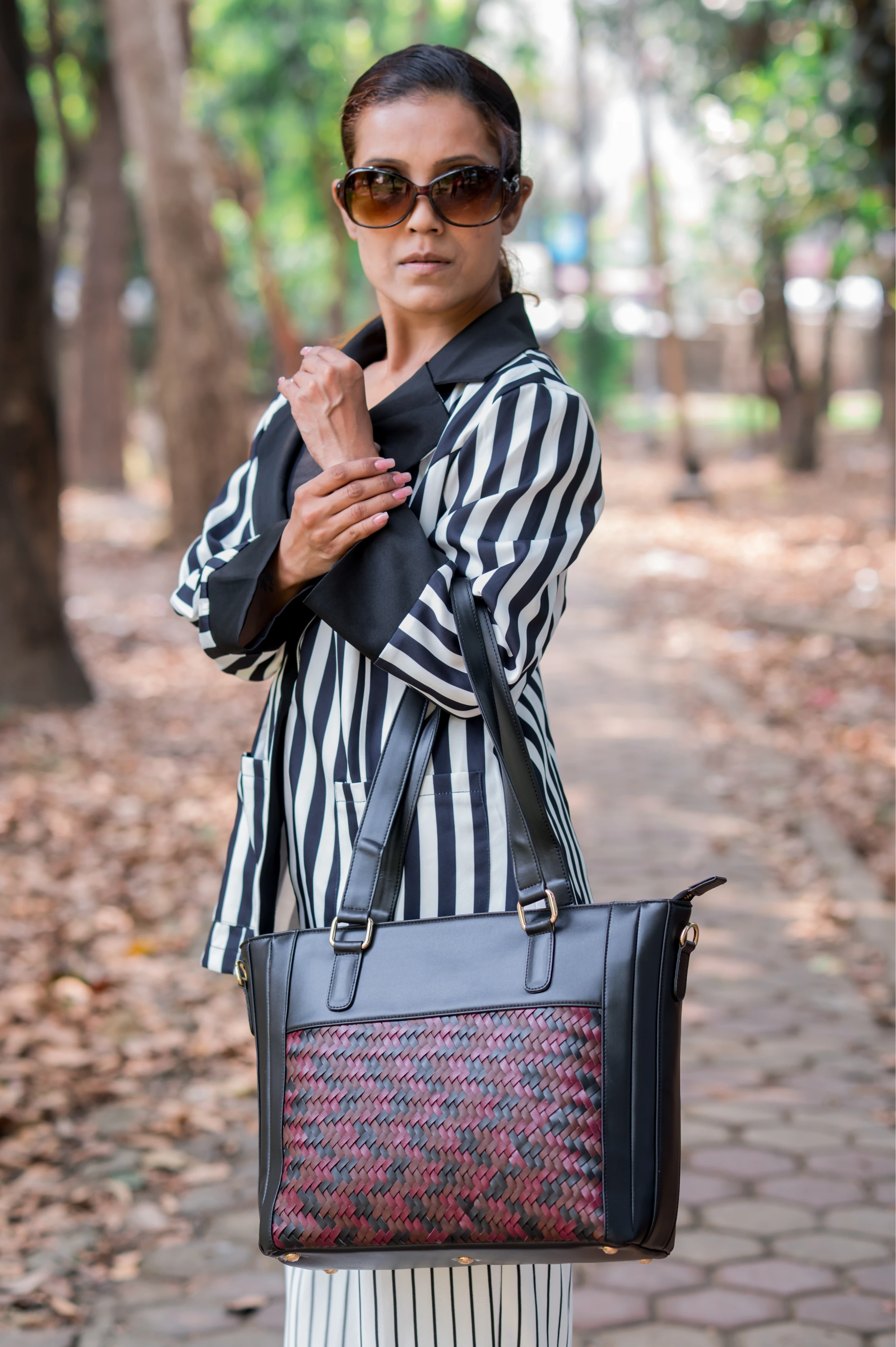 Woman holding a black vegan leather handbag for women with a patterned design in an outdoor setting