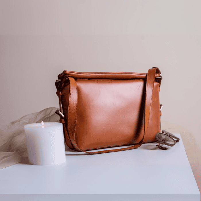 Brown vegan leather handbag for women on a light surface with a white candle and beige fabric in the background.