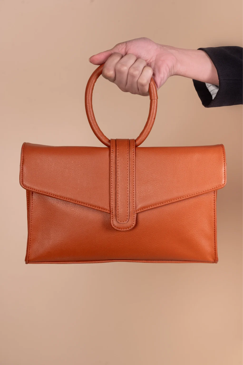 Hand holding a brown leather vegan handbag for women against a beige background