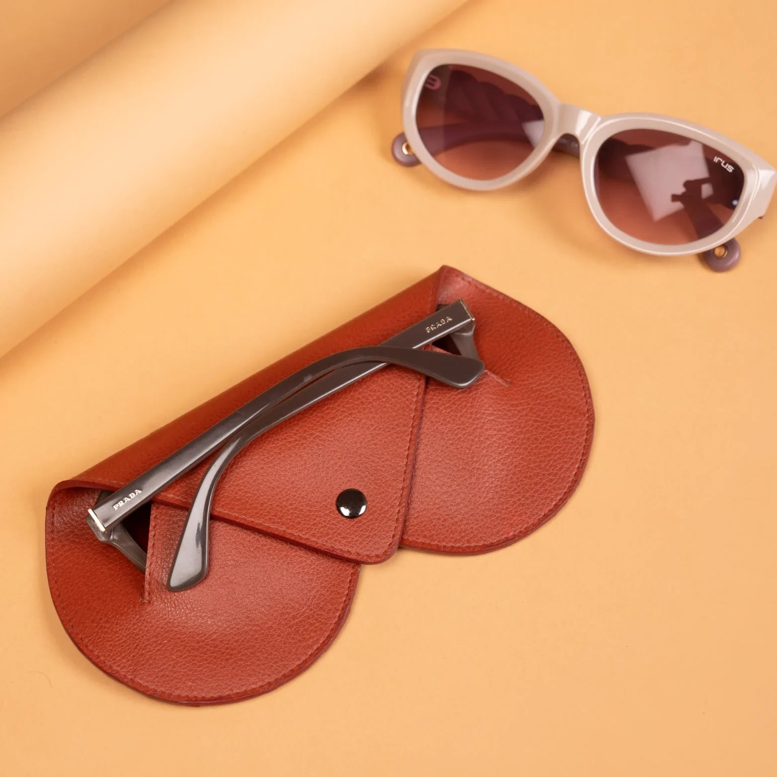 Brown vegan leather case with nail clippers and sunglasses on a beige background