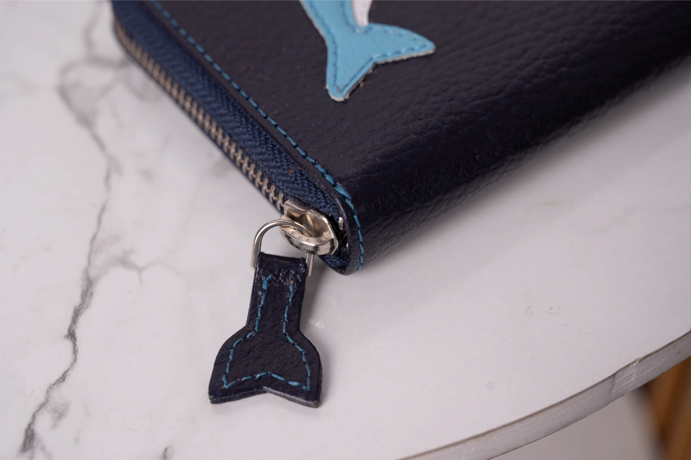 Black vegan leather wallet for women with blue whale charm on a marble surface