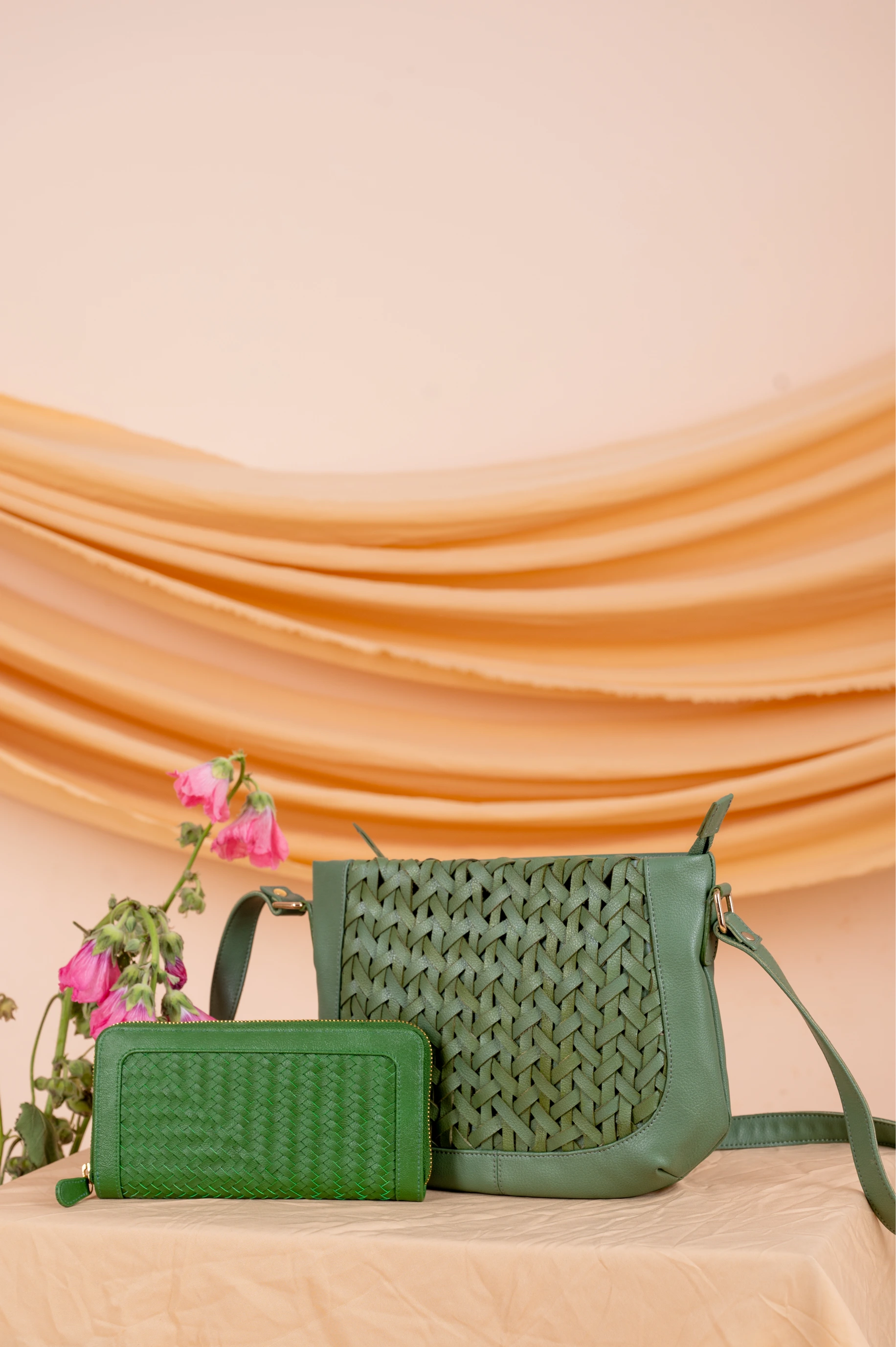 Green woven vegan leather handbag for women and vegan leather wallet for women on a beige surface with a draped fabric background
