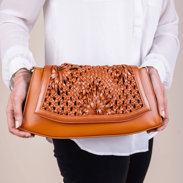 Brown woven vegan leather clutch for women held by a person wearing a white shirt against a beige background