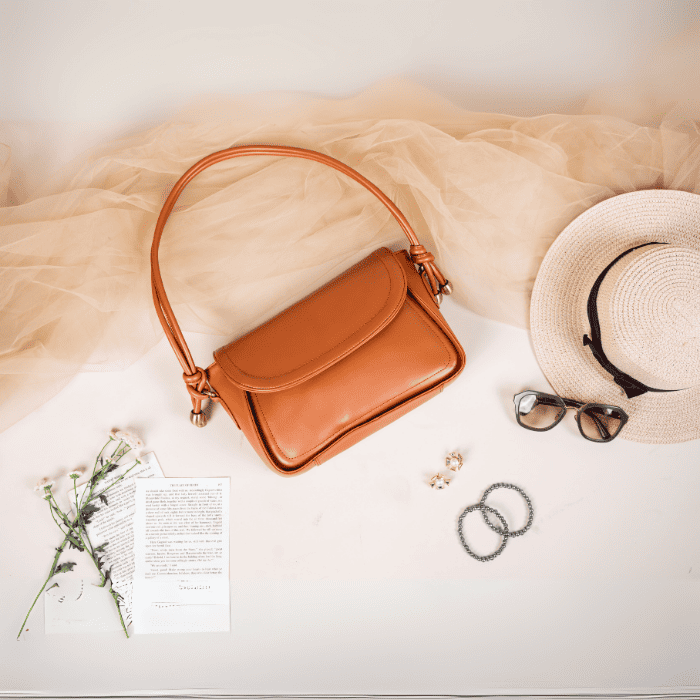 Brown vegan leather handbag for women with a hat, sunglasses, and jewelry on a light background