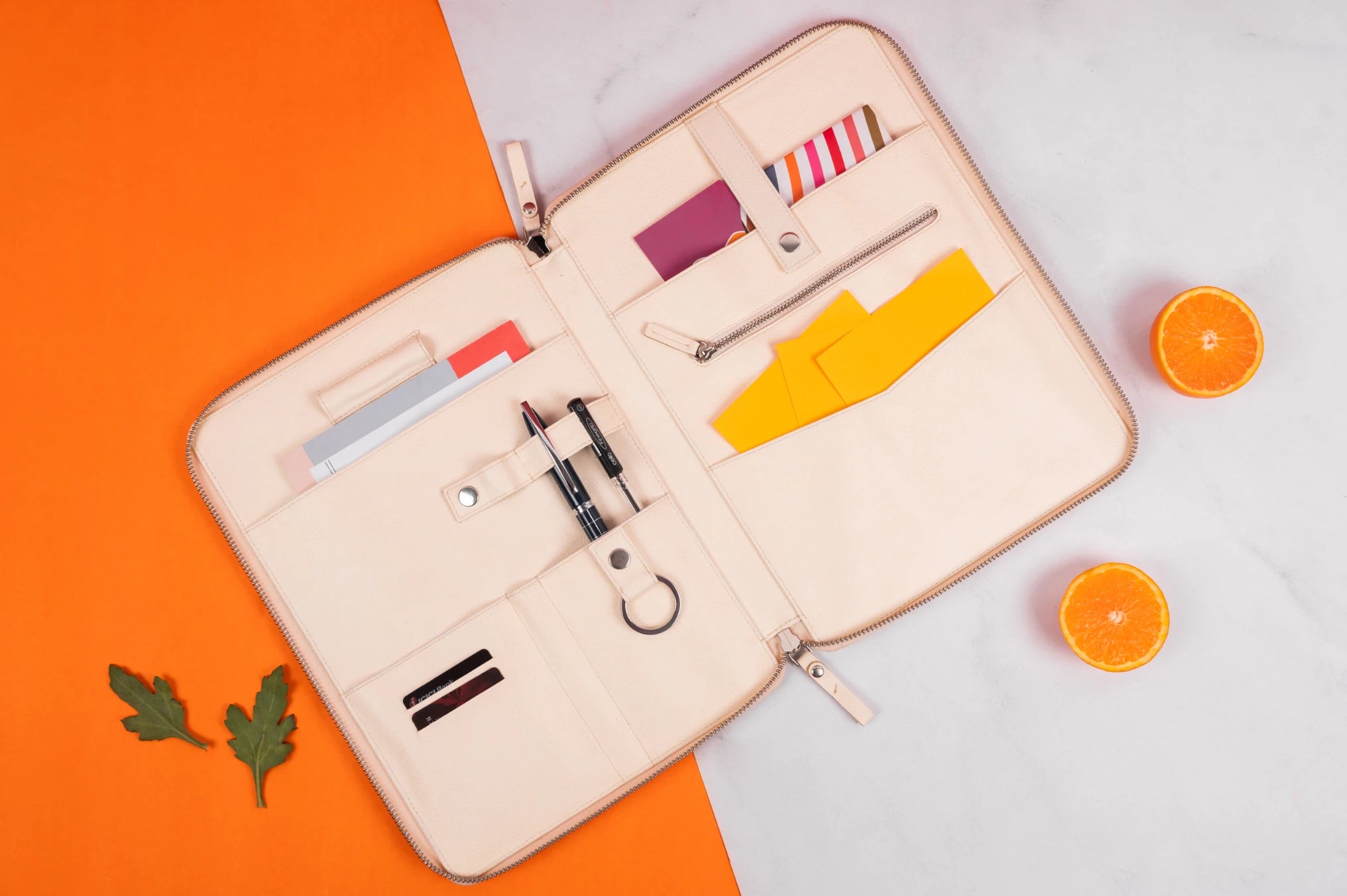Open beige vegan leather travel organizer with compartments on an orange and white background