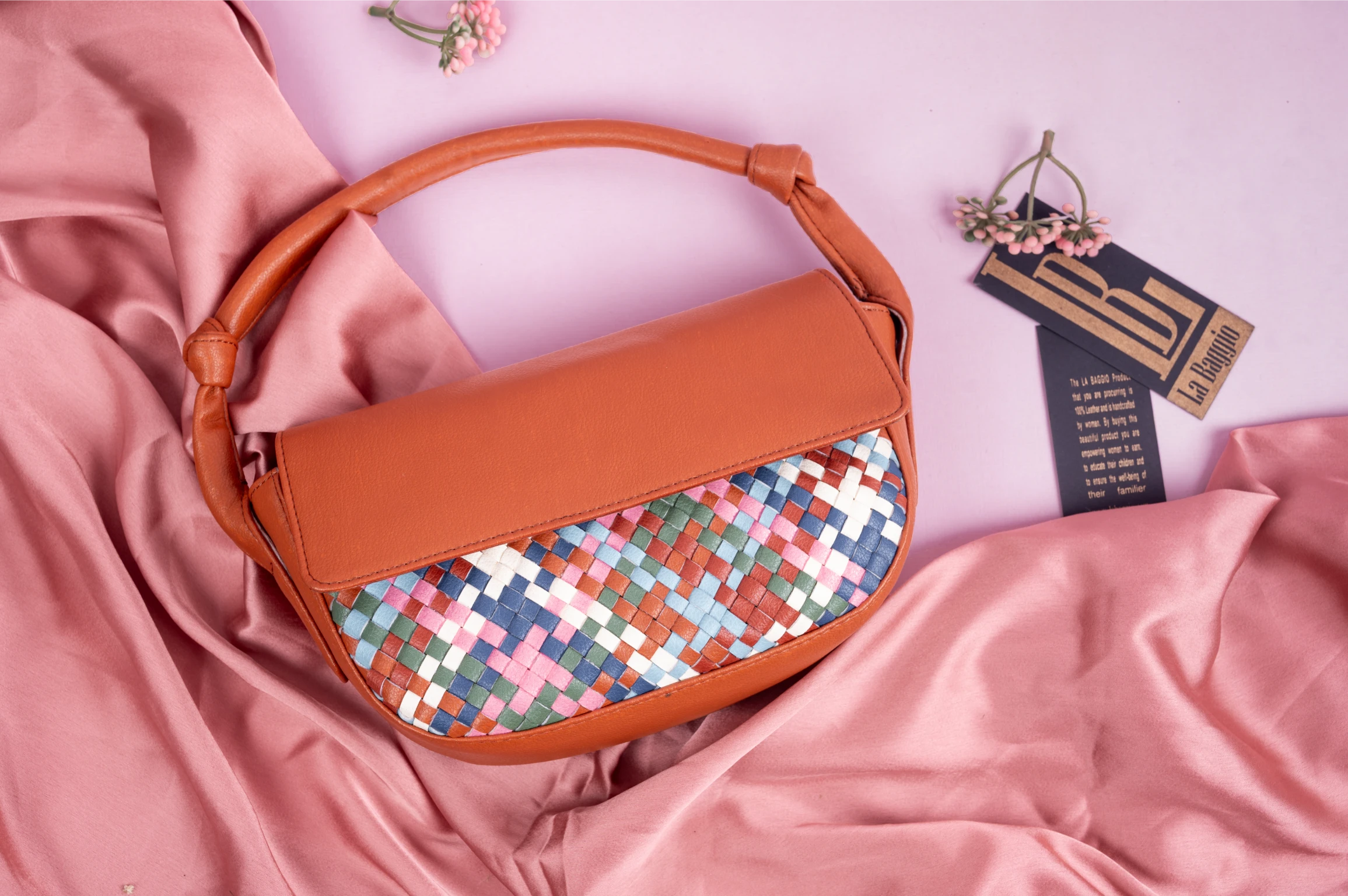 Brown vegan leather handbag for women with a colorful woven pattern on a pink fabric background
