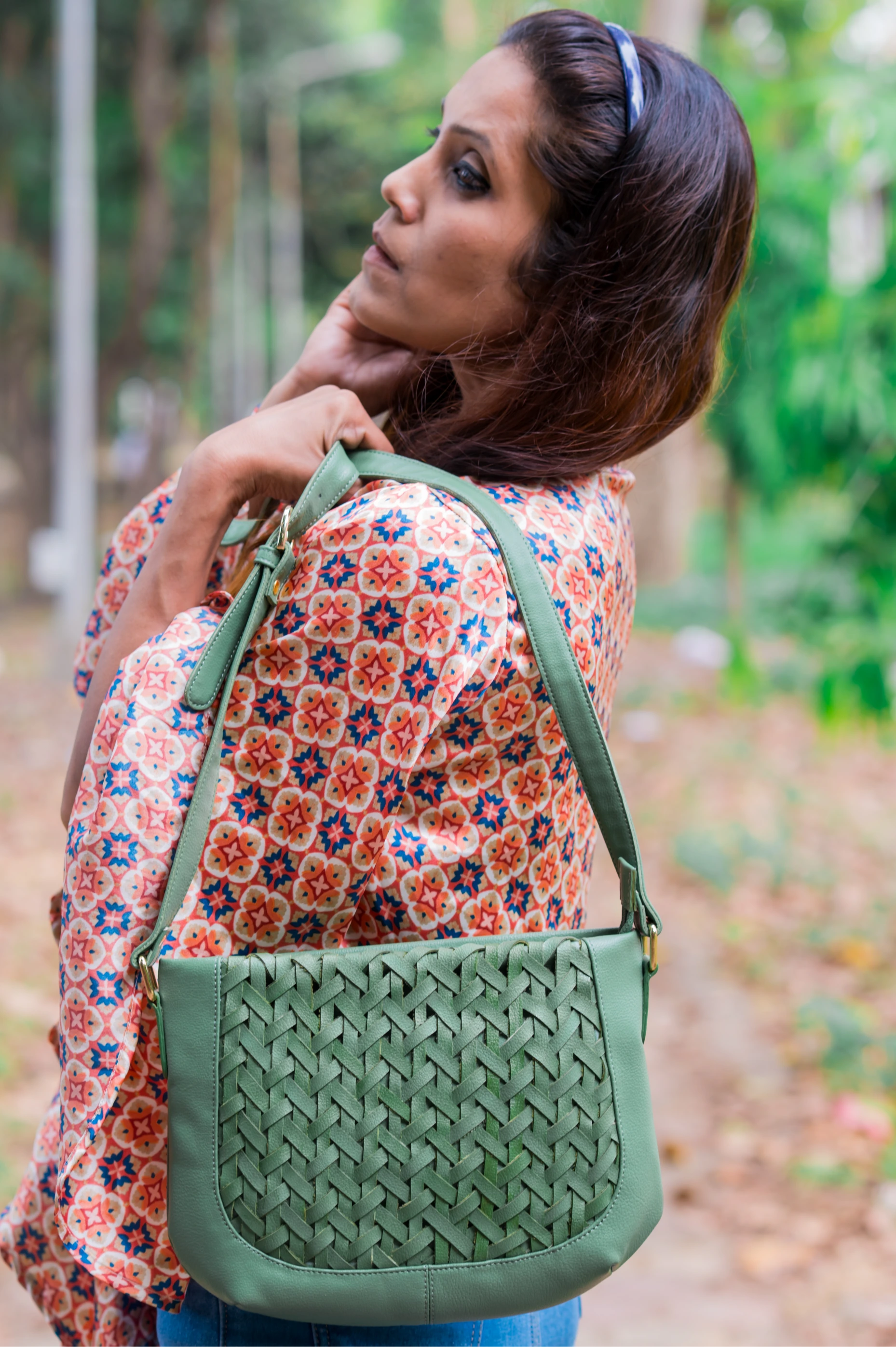 Woman holding a green woven vegan leather handbag for women in a forest setting