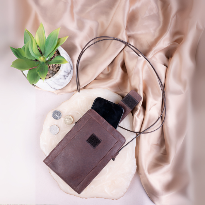 Brown vegan leather pouch with phone and coins on a beige fabric background