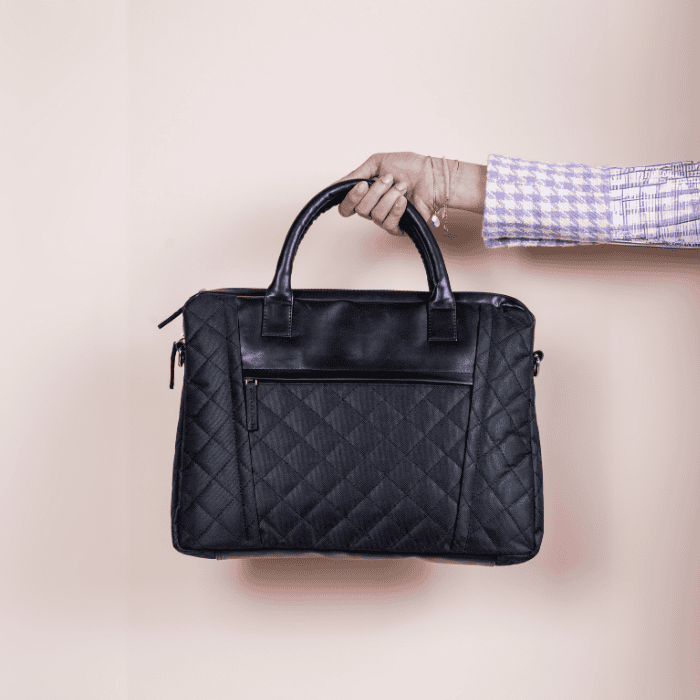 Black quilted vegan leather laptop bag held by a hand on a beige background