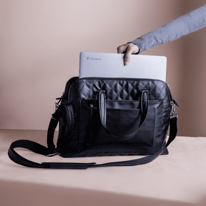 Black quilted vegan leather handbag for women with a laptop inside, held by a person's hand against a beige background