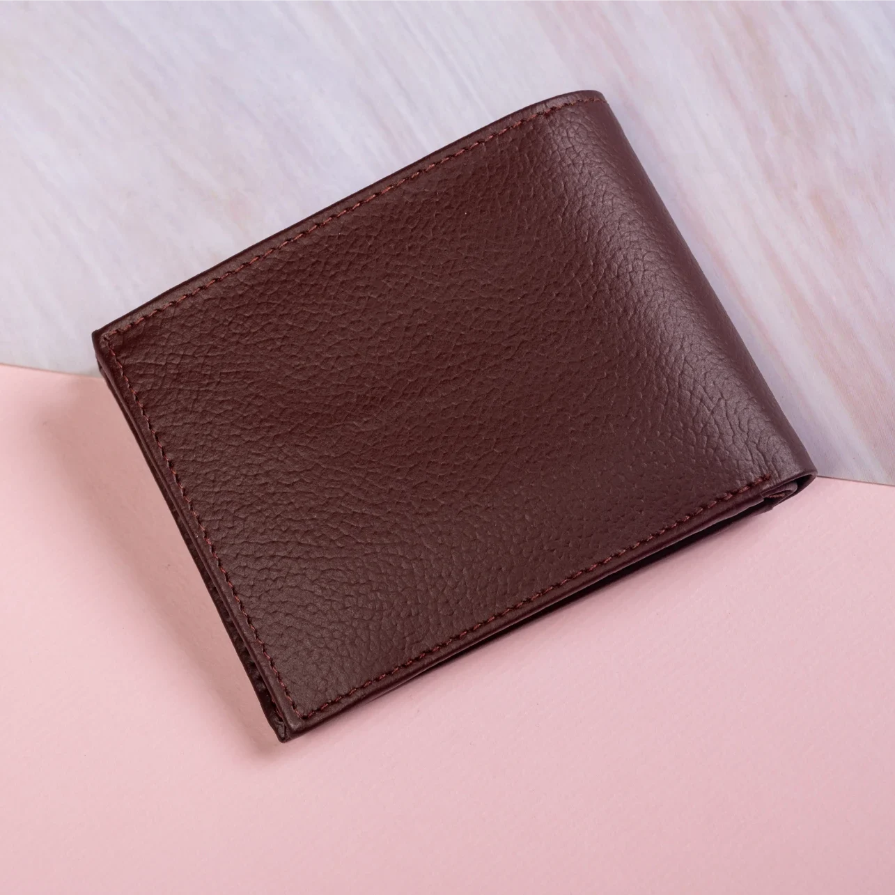 Brown leather wallet for men on a light pink surface with a blurred white background