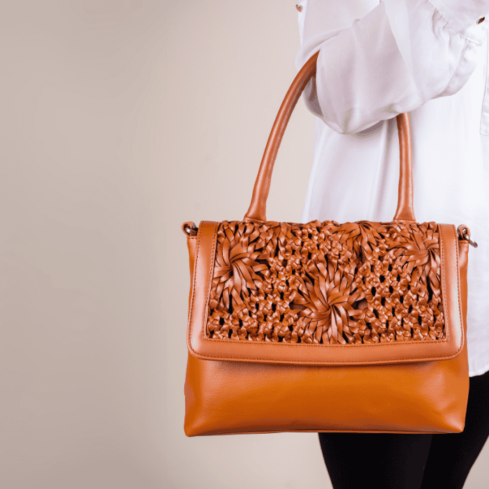 Brown vegan leather handbag for women with intricate carvings held by a person wearing a white shirt.