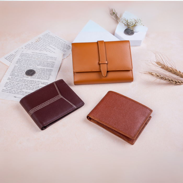 Three brown vegan leather wallets for men on a light pink surface with papers and dried plants.