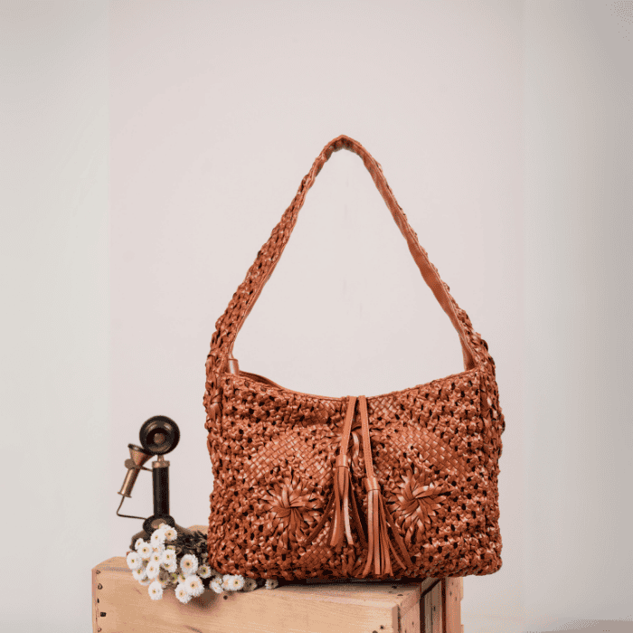 Brown woven vegan leather handbag for women with tassels on a wooden surface against a light background
