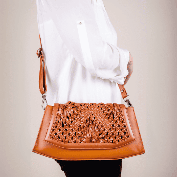 Brown woven vegan leather handbag for women held by a person wearing a white shirt against a neutral background