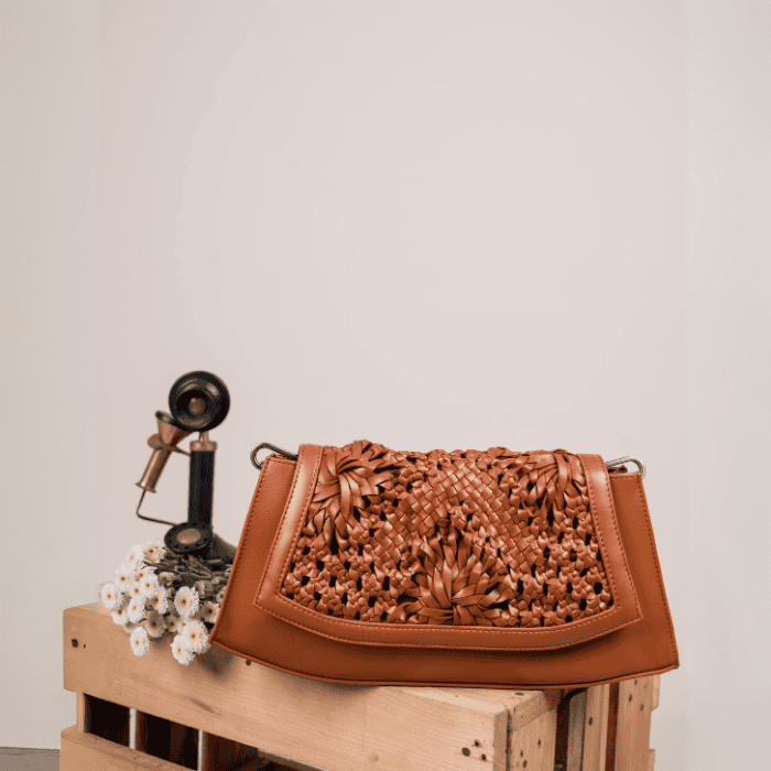 Brown woven vegan leather handbag  for women on a wooden crate with a vintage phone and flowers against a beige wall.