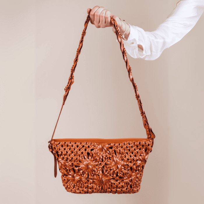 Brown woven vegan leather handbag for women held by a person against a beige background