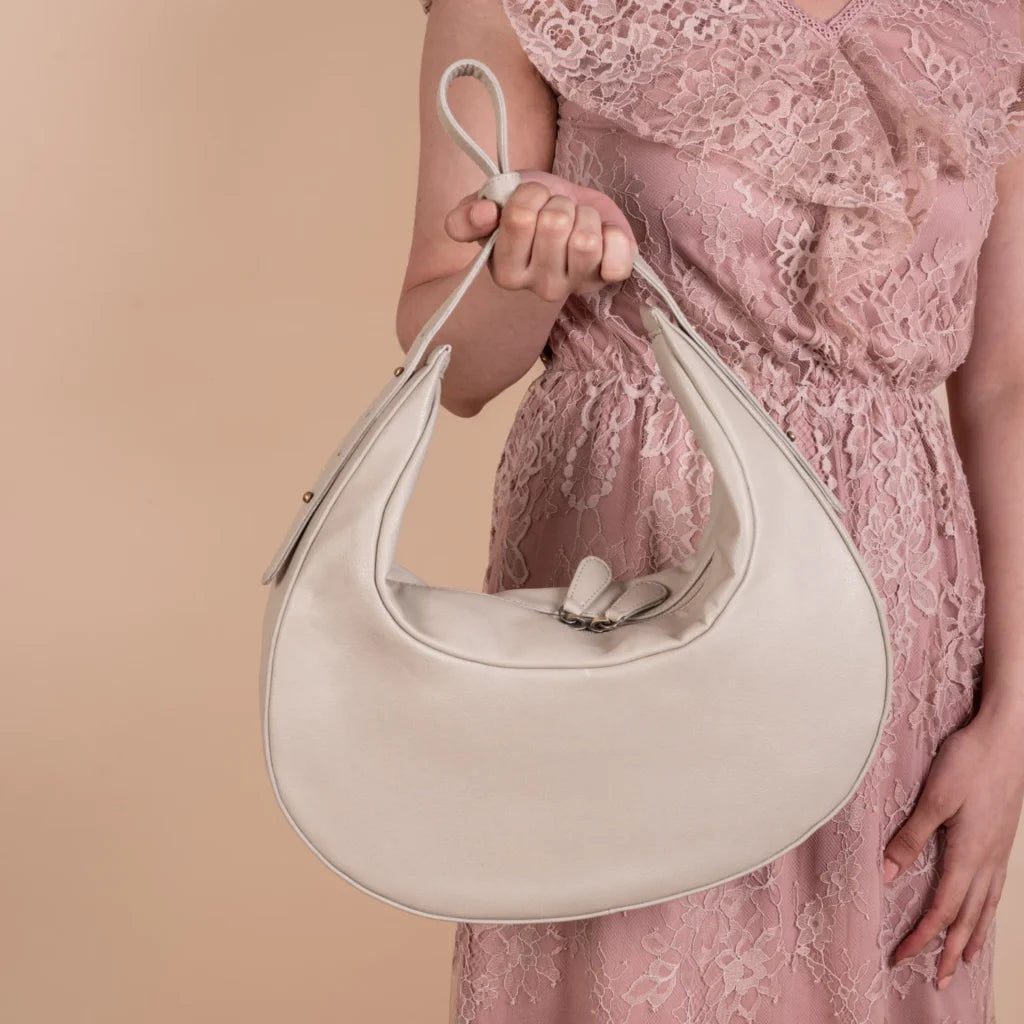 Person holding a white vegan leather handbag for women with a pink lace dress against a beige background