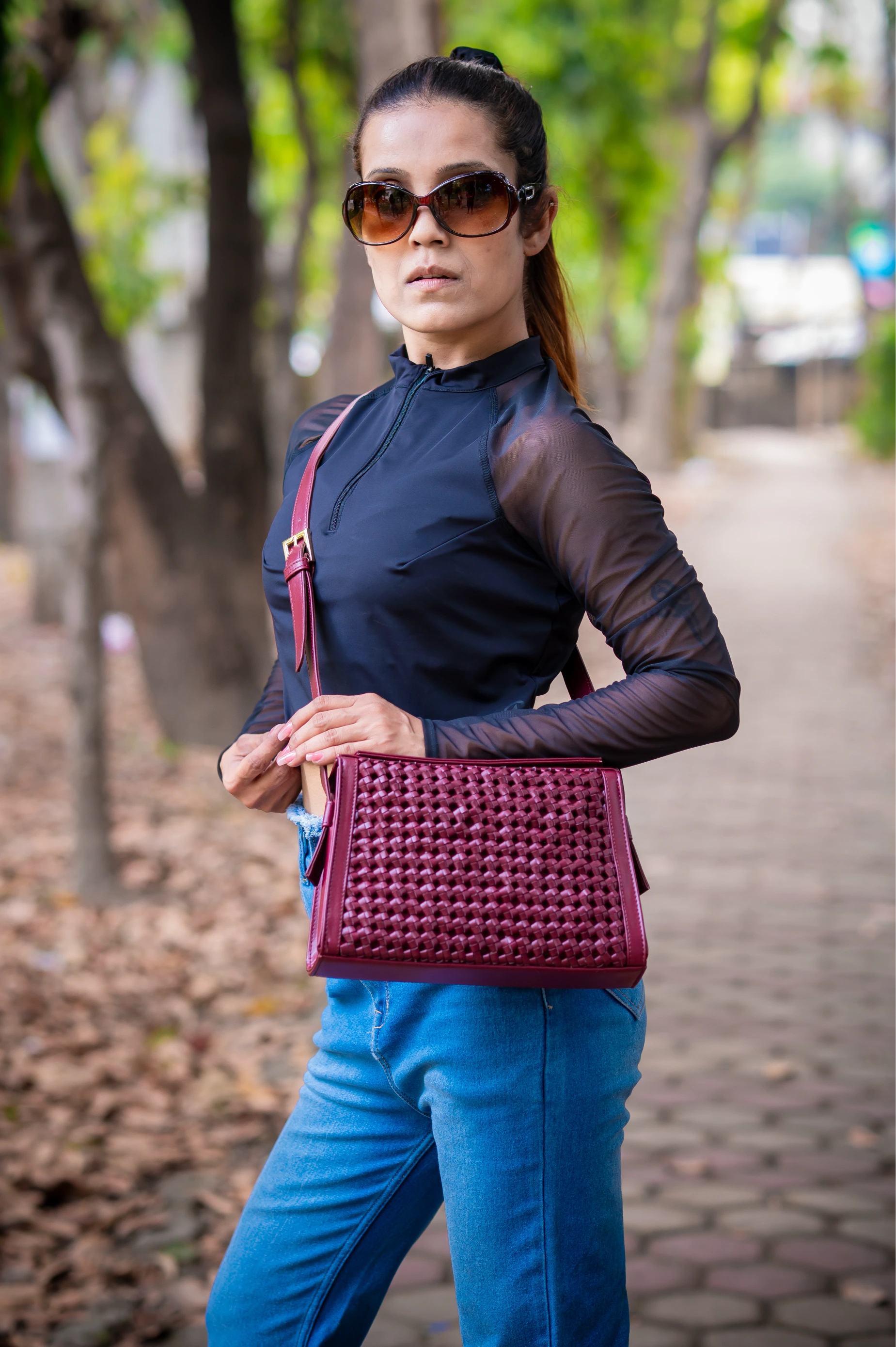 Woman walking outdoors wearing sunglasses and a dark top with a red vegan leather woven handbag for women