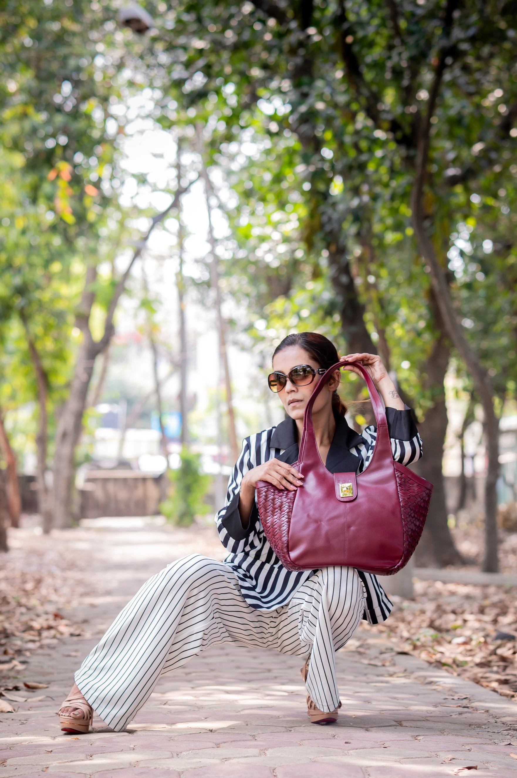 Woman holding a maroon vegan leather handbag for women in a park setting