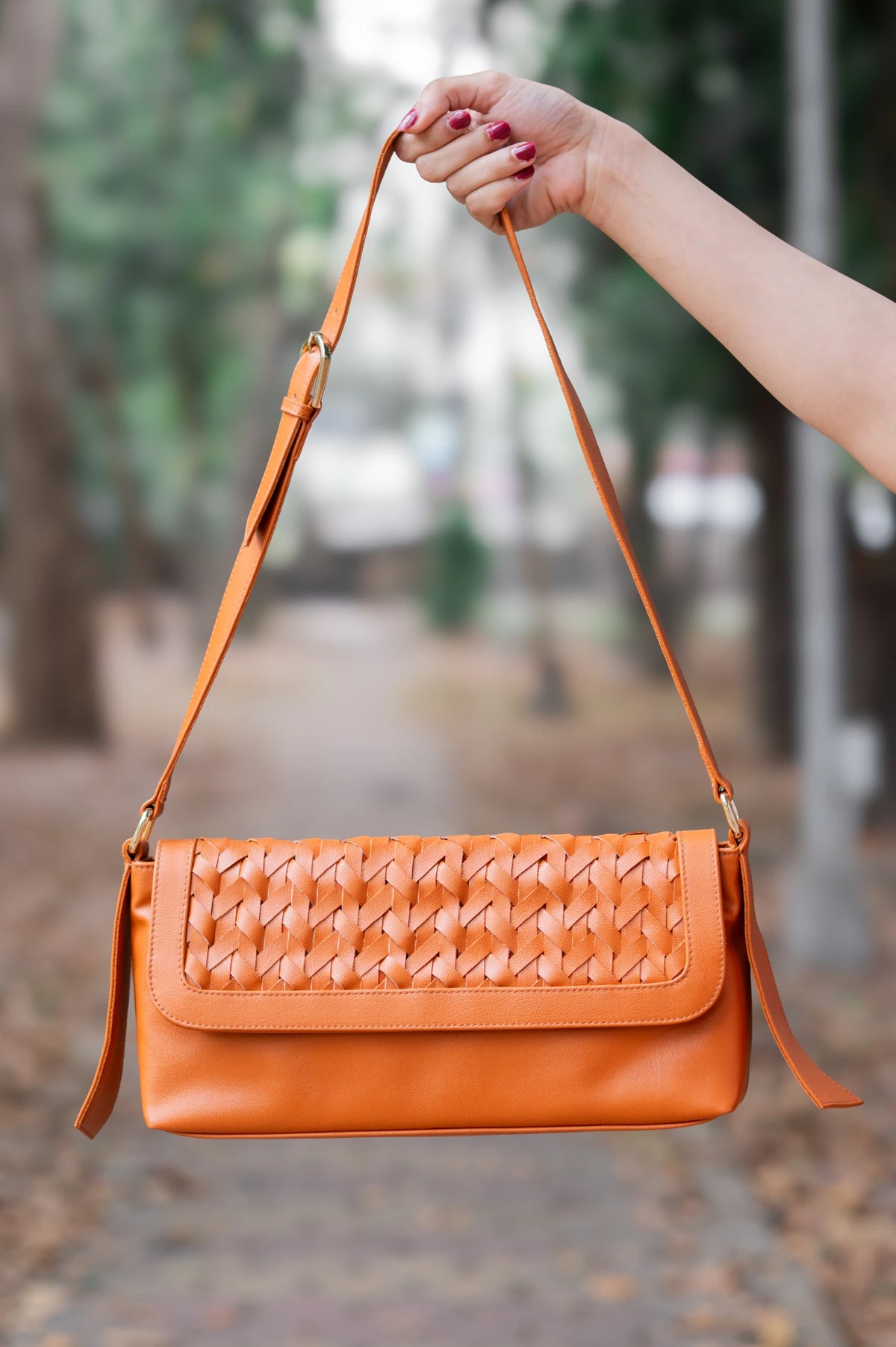 Orange woven vegan leather handbag for women held by a hand with a blurred outdoor background