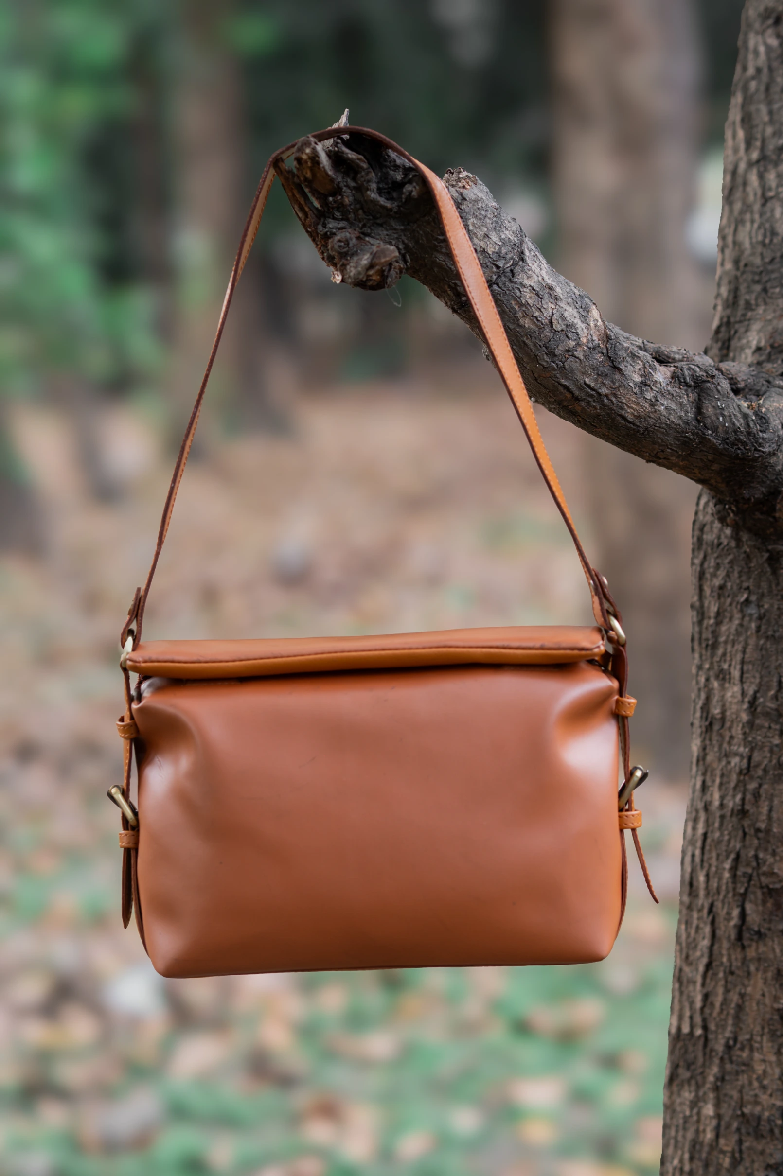 Brown leather vegan leather handbag for women hanging on a tree branch with a natural background