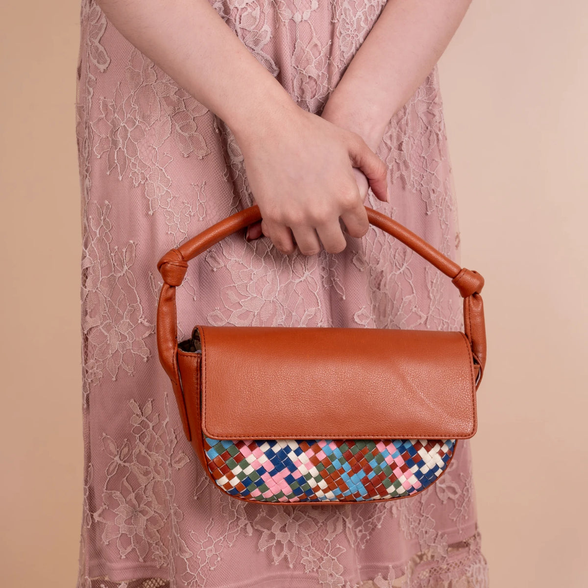 Brown vegan leather handbag for women with a colorful woven pattern held by a person wearing a pink lace dress.