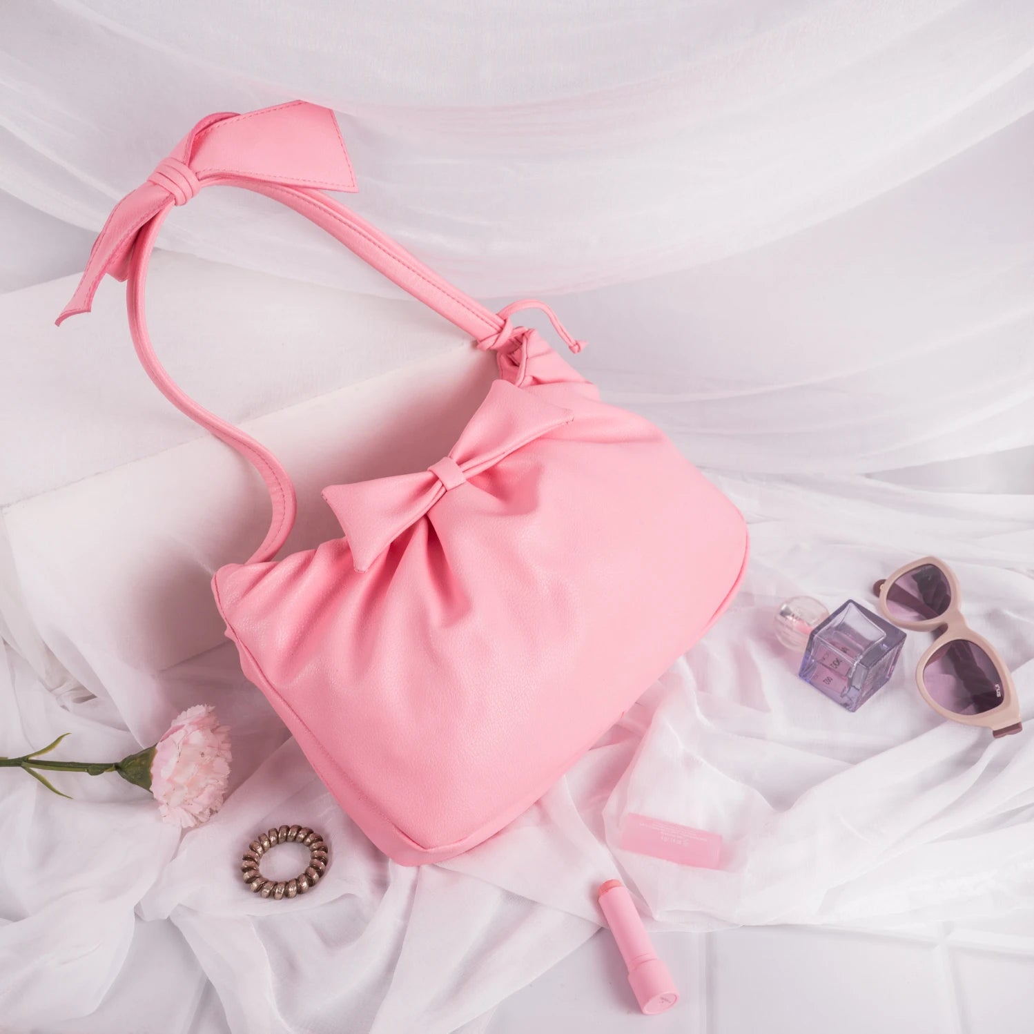 Pink vegan leather bag for women with accessories on a white fabric background