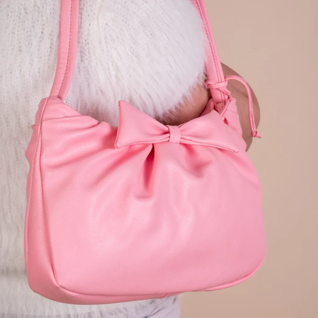 Pink vegan leather handbag for women with a bow held by a person against a neutral background