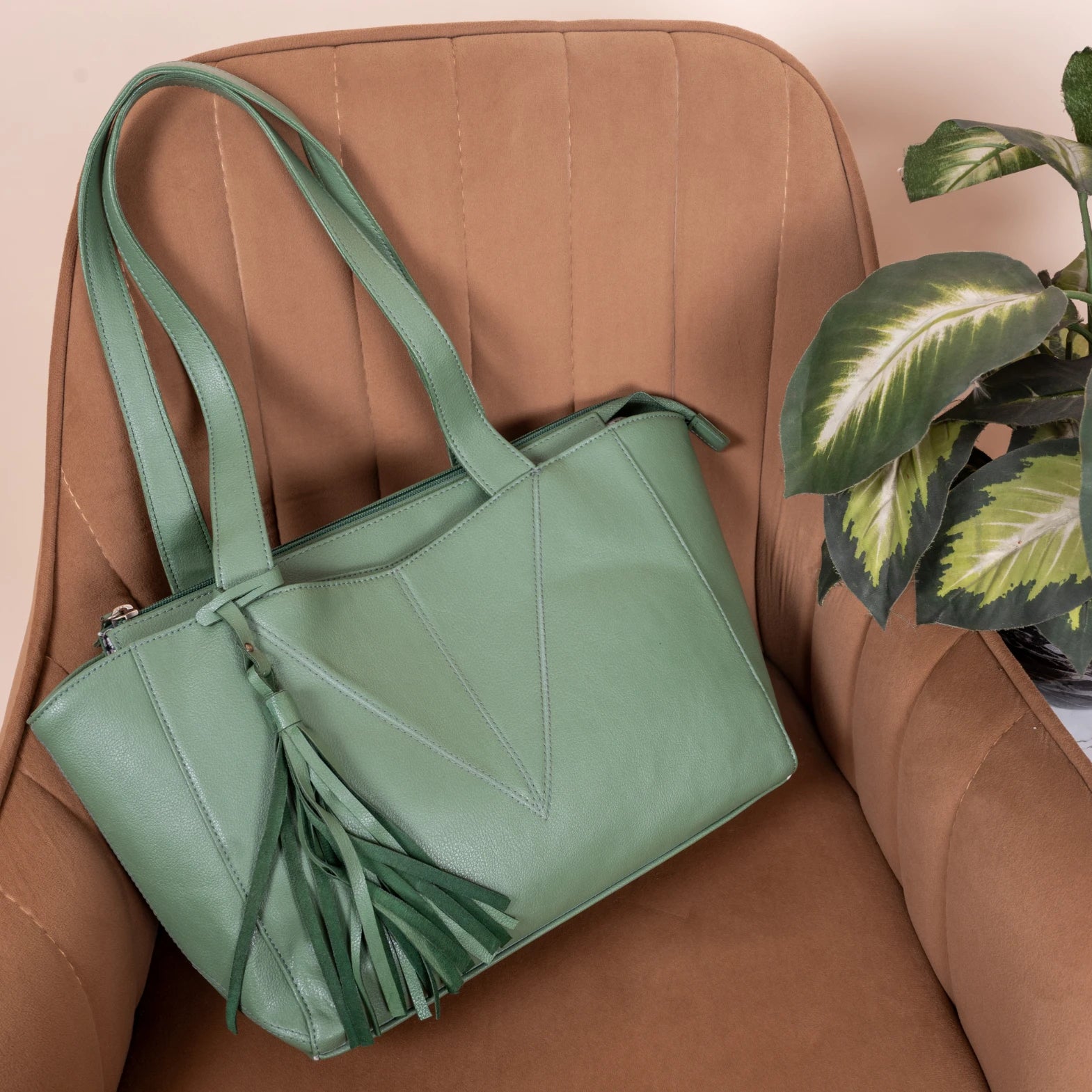 Green vegan leather handbag for women with tassel on a brown chair with a plant in the background