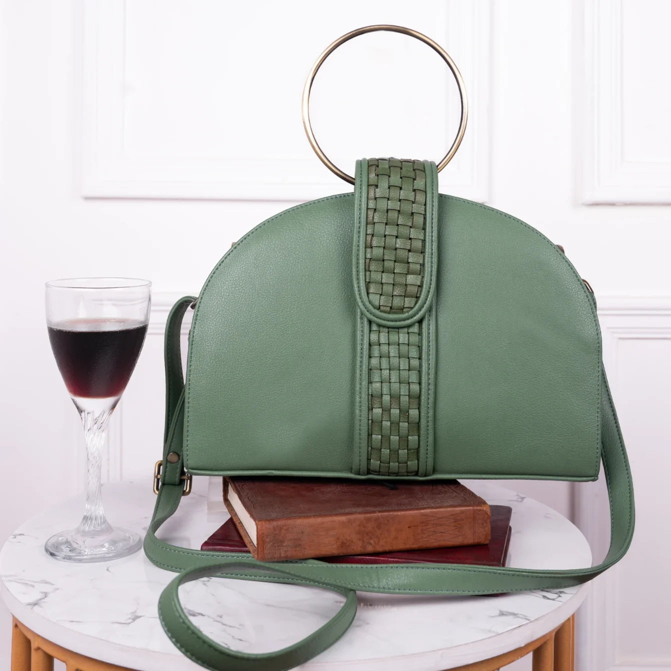 Green vegan leather handbag for women with woven detail on a white surface with a glass of red wine and books.