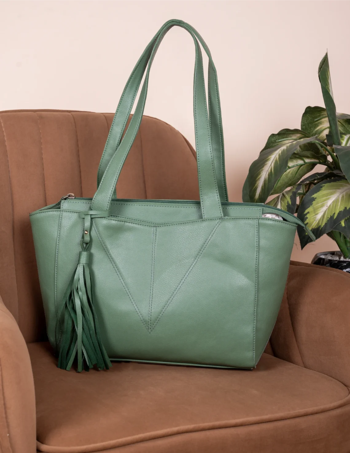 Green vegan leather handbag for women with a tassel on a brown chair
