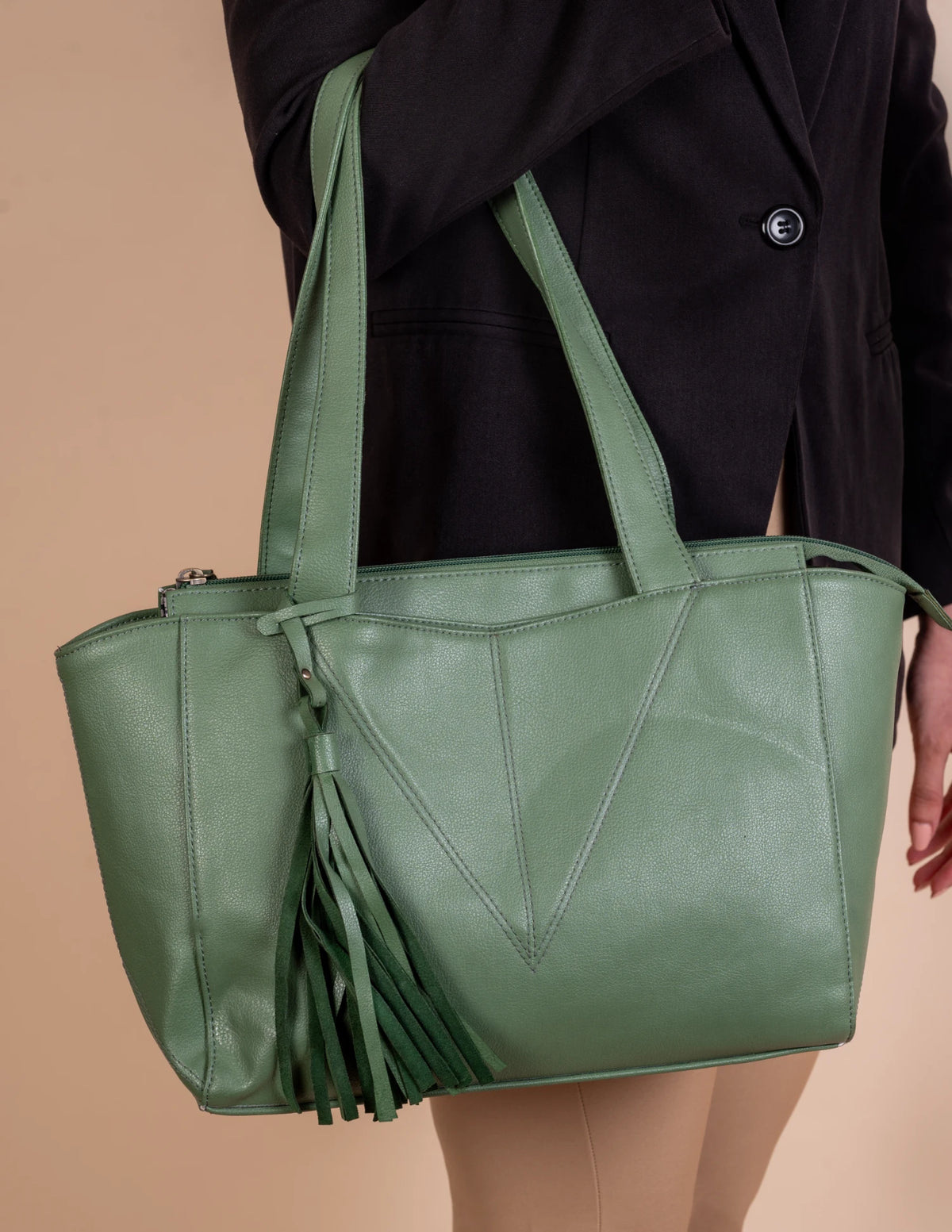 Green vegan leather tote bag for women with tassels held by a person against a beige background