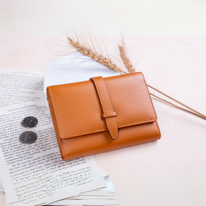 Brown vegan leather wallet on an open book with dried plants on a light background