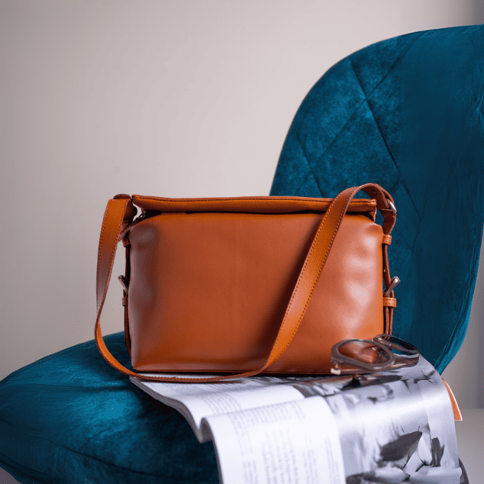 Brown vegan leather handbag for women on a blue chair with a magazine underneath