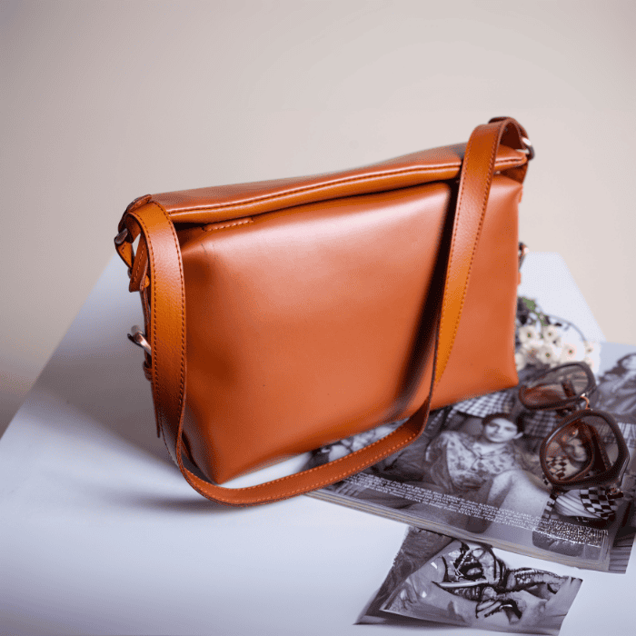 Brown vegan leather handbag for women on a light surface with a magazine underneath