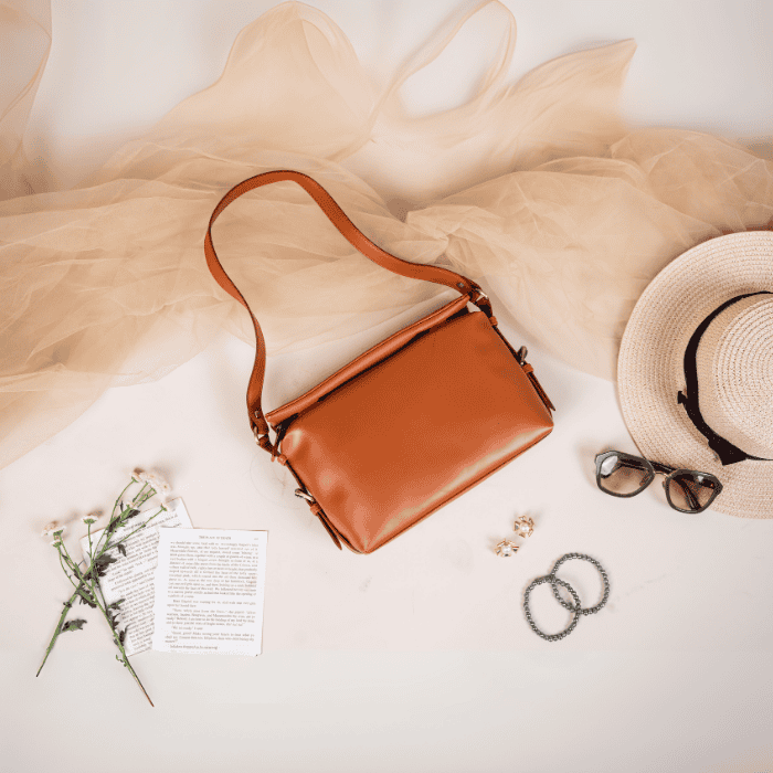 Brown vegan leather handbag for women with a hat, sunglasses, and flowers on a light background