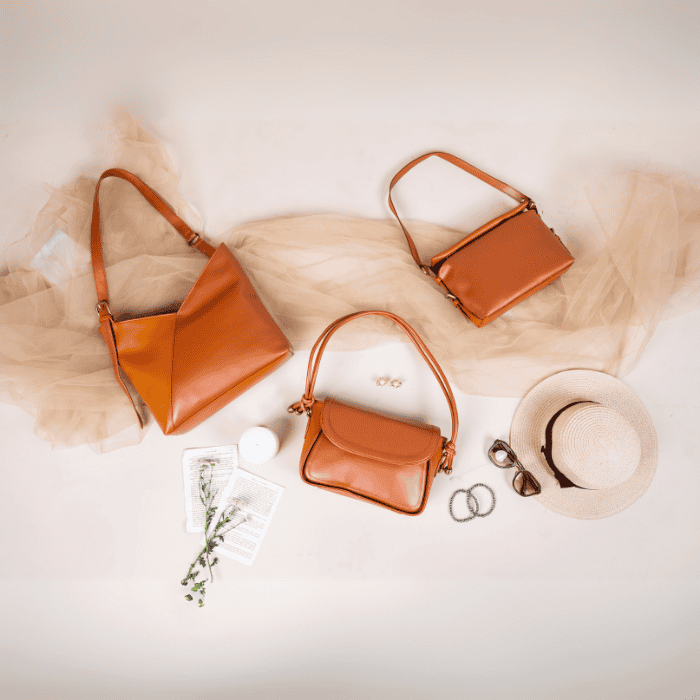 Three brown vegan leather handbags for women on a textured surface with a hat and sunglasses.