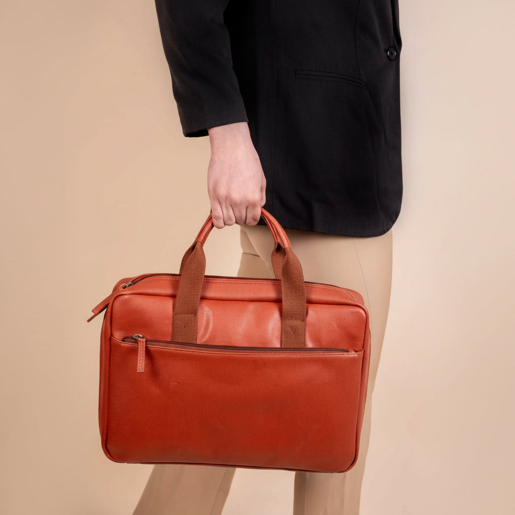 Person holding a red vegan leather laptop bag against a beige background