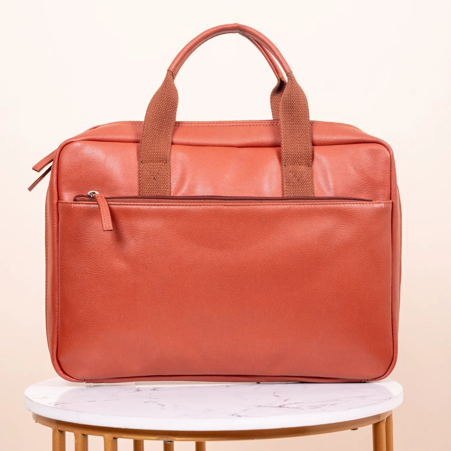 Brown vegan leather laptop bag on a white surface with a beige background